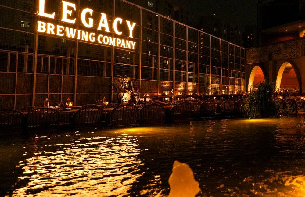 Fountain water reflecting the Legacy Brewing Company sign at night
