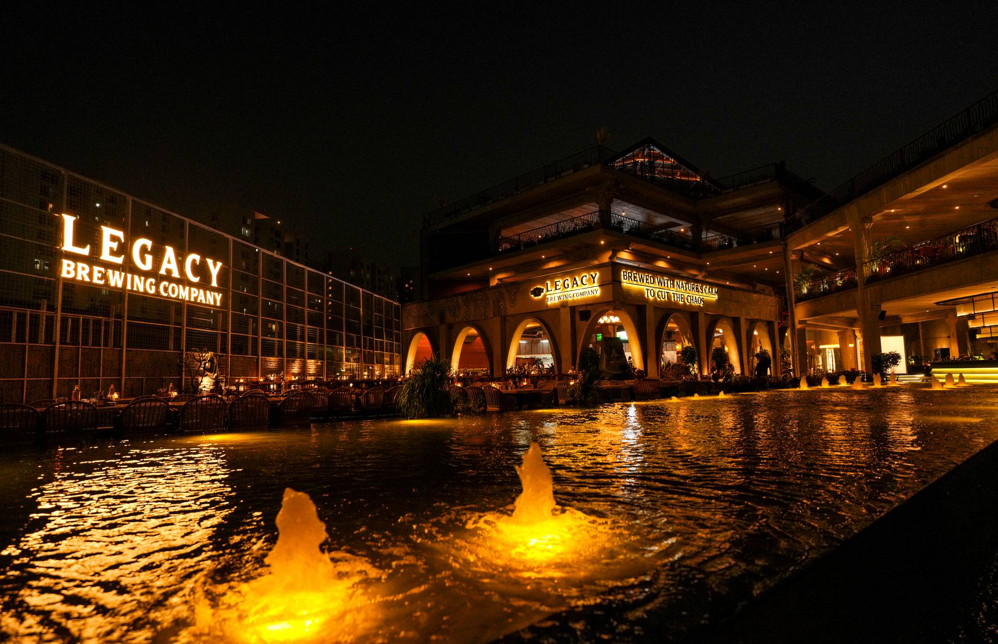 Legacy Brewing Company illuminated at night beside its fountain plaza